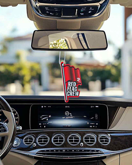 Car interior with Red Flag Crew air freshener hanging from rearview mirror.